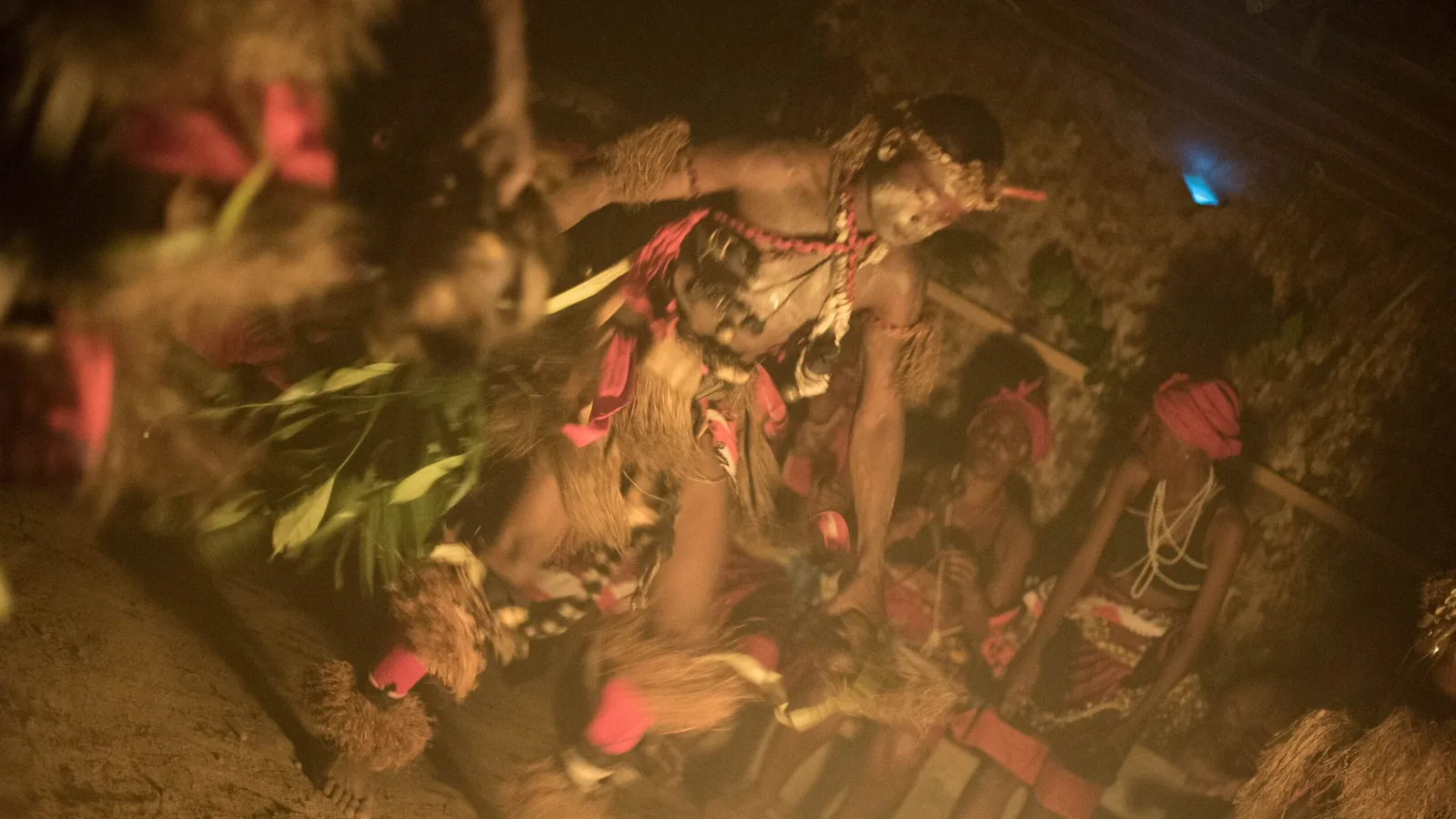 Bwiti dancers in raffia and red paint moving around the fire in a temple in Gabon