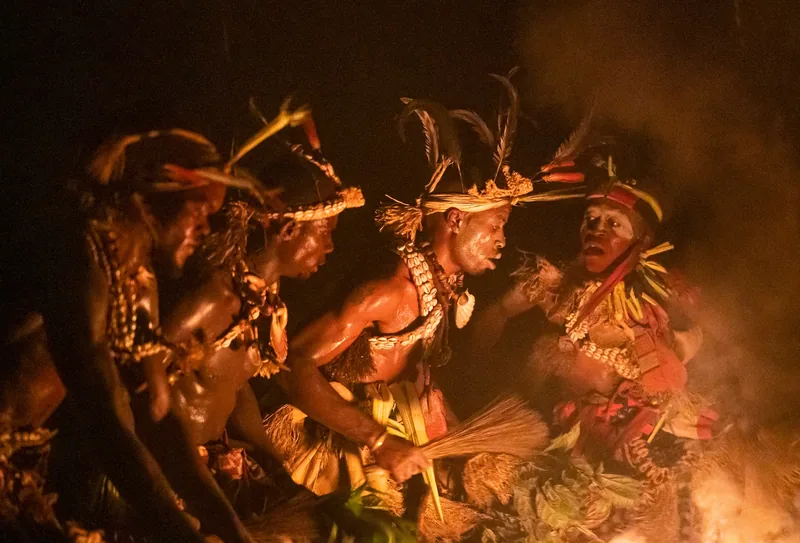 Missoko Bwiti practitioners in feathers and cowrie shells dancing around the fire at night in Gabon