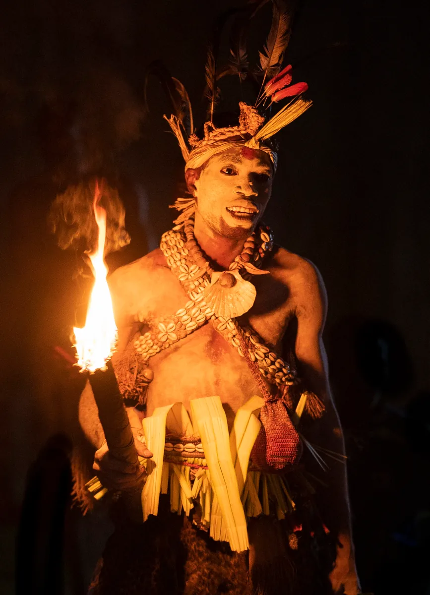 A Missoko Bwiti practitioner in ceremonial dress holding a torch during a night ceremony in Gabon