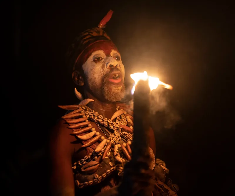 A Missoko Bwiti practitioner with white face paint singing by torchlight during a night ceremony in Gabon