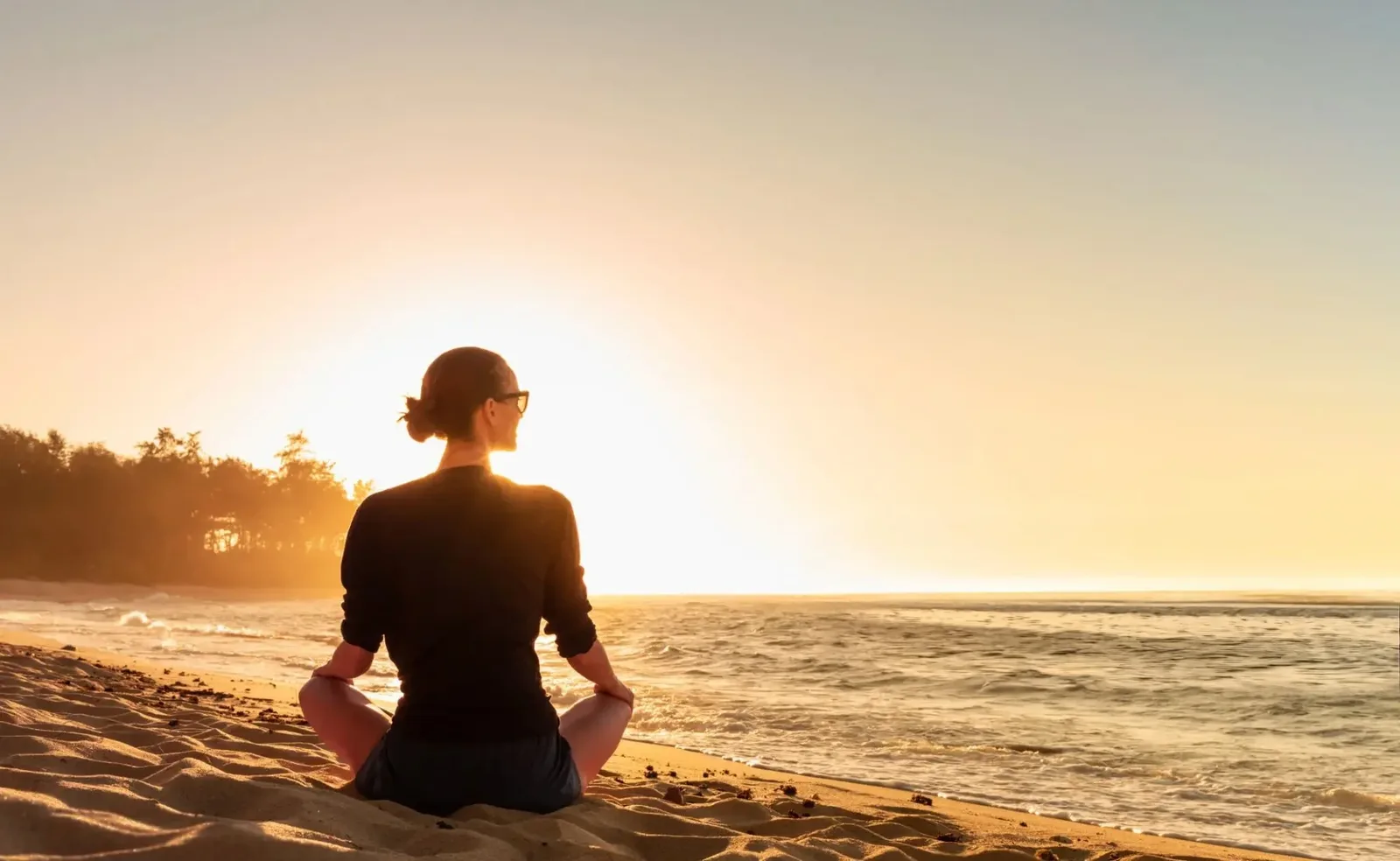 A person sitting in meditation on a beach at sunrise