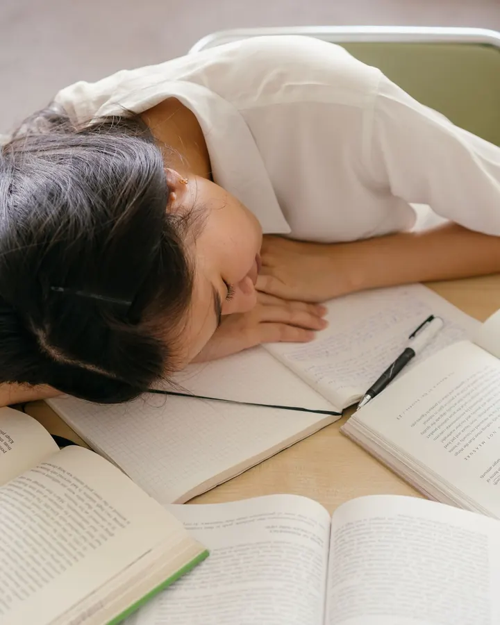 A student asleep with her head on open books at a desk